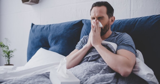 man sneezing in bed